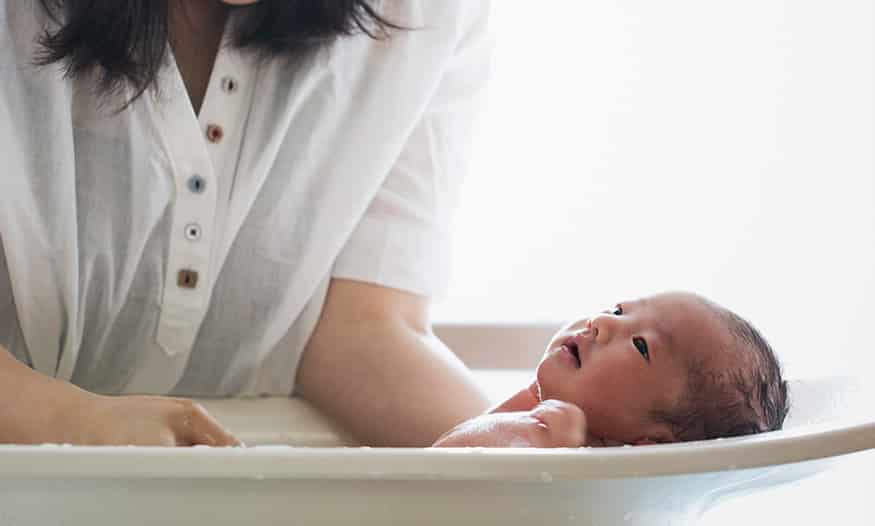 mamá sujeta a bebé dentro de la bañera